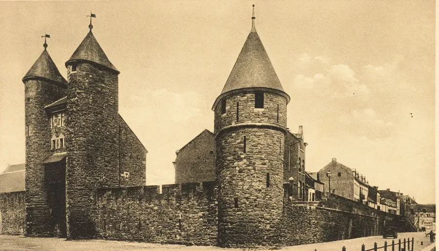 明信片:左边是 Helpoort(地狱门),两座圆塔顶着尖屋顶,旁边是城墙的城垛;右边是粗壮的圆形 Jekertoren 塔楼,顶着锥形屋顶。右侧的城墙沿着一排房屋延伸出去。